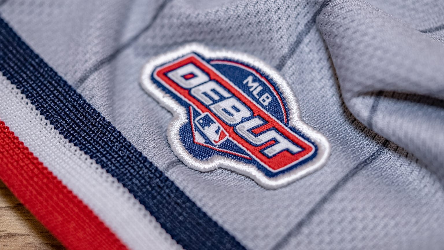 The MLB Debut patch, embroidered on a grey jersey: DEBUT in red and white with the MLB logo, on a navy shield.